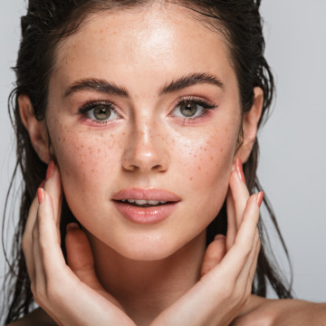 Junge brünette Frau berührt begeistert faltenfreies Gesicht nach Faltenbehandlung